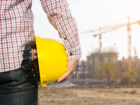 Hand's engineer worker holding yellow safety helmet with building on site background.